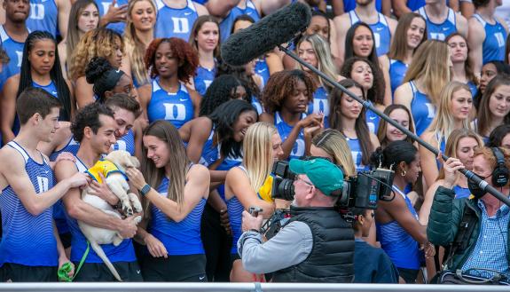 A 60 Minutes film crew captures members of the Duke track team embracing a kindergarten puppy. Photo by Jared Lazarus