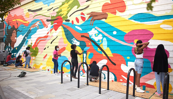 Arce (center, in Black) works on the mural with a group of students.