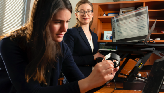 Ph.D. student Brinnae Bent prepares to download information from a wearable health monitoring device while assistant professor Jessilyn Dunn looks on. (Les Todd)