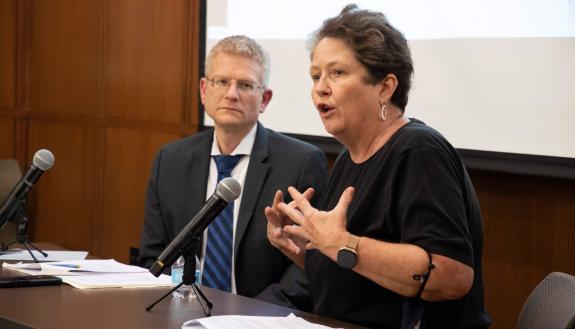 Professor Robin Kirk is seated at a table with professor Neil Siegel. Kirk is speaking and gesturing with her hands.