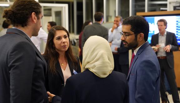 Four individuals in business attire speak in a huddle at a conference.