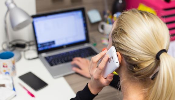 A woman talks on her phone while also using her computer.