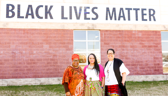 Photo of three black women pastors in front of Black Lives Matter mural