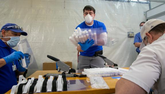 Three people assemble face shields.