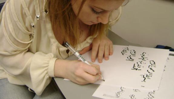 A student writes out an Arabic phrase.  