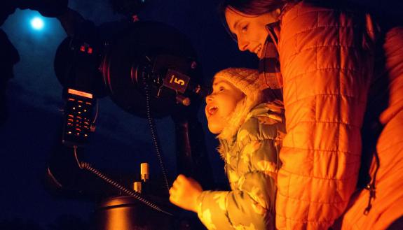 Maura Farver of Durham holds Poppy Overman, 3, in awe as she views the moon's craters through a telescope at the Duke Teaching Observatory in Duke Forest. Photo by Jared Lazarus, Duke University.