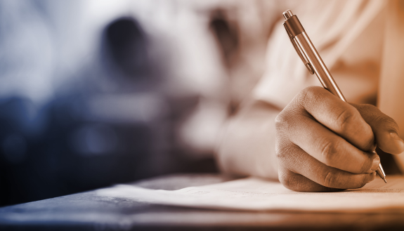 image of student writing at a classroom desk