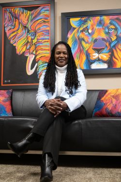 Ashleigh Shelby Rosette, a senior associate dean at the Fuqua School of Business, sits on a black couch in front of colorful artwork of an elephant and a lion..